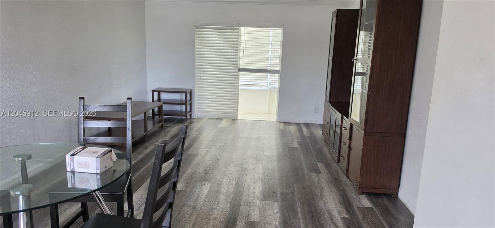 This living and dining area features wood-look flooring, a glass table, and a sliding door — AVENTURA, FL