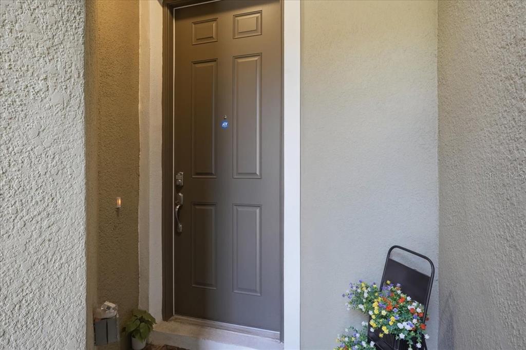 A brown front door with an ADT security sticker sits in a stucco entryway — 34179 CINDER WAY, WESLEY CHAPEL, FL