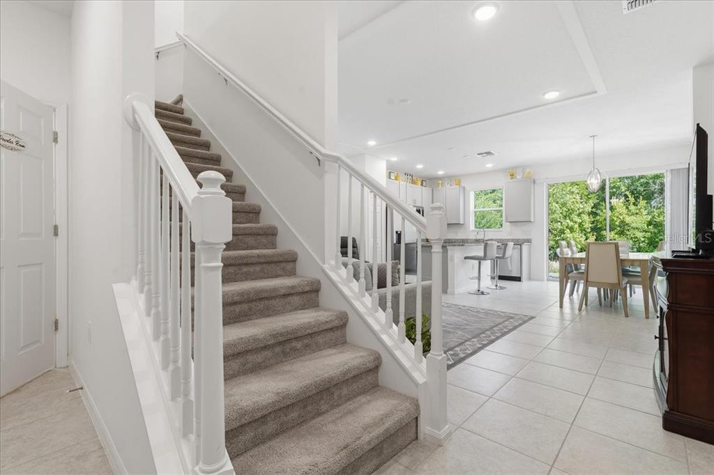 A carpeted staircase leads to an open-concept kitchen and dining area with tile flooring — 34179 CINDER WAY, WESLEY CHAPEL, FL