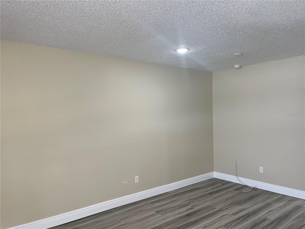 An empty room features beige walls, gray wood-look flooring, and a white popcorn ceiling — 9105 TUDOR DRIVE UNIT F103, TAMPA, FL