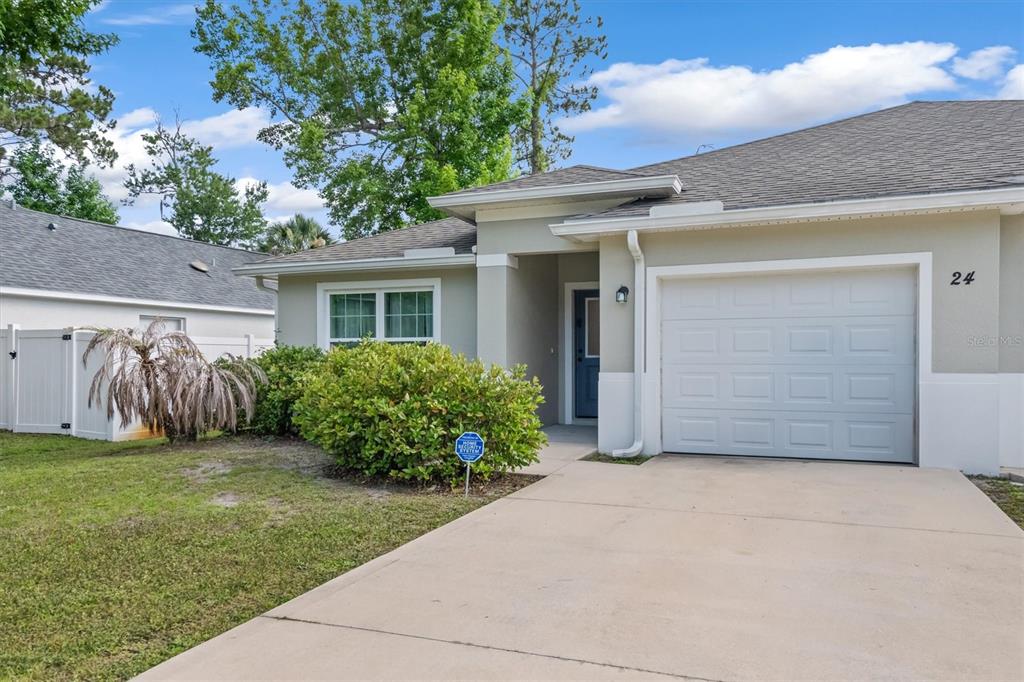 A single-story house exterior features a concrete driveway, a white garage door, and landscaping — 24 PONTIAC LANE, PALM COAST, FL