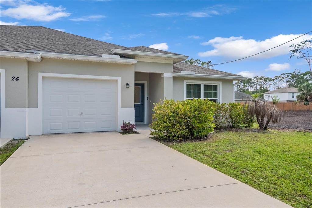 A single-story house with a white garage, a blue front door, and a concrete driveway — 24 PONTIAC LANE, PALM COAST, FL