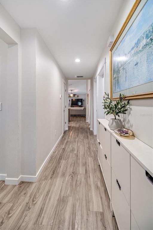 A hallway with light wood-look flooring leads to a living area with a television — 24 PONTIAC LANE, PALM COAST, FL