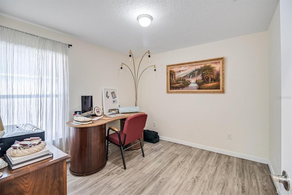 A home office features wood-look flooring, a curved desk, a red chair, and wall art — 24 PONTIAC LANE, PALM COAST, FL