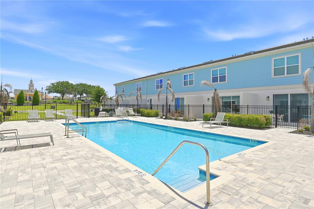 A rectangular swimming pool sits on a paved patio beside a two-story blue building — 7857 SPECTRUM DRIVE, REUNION, FL