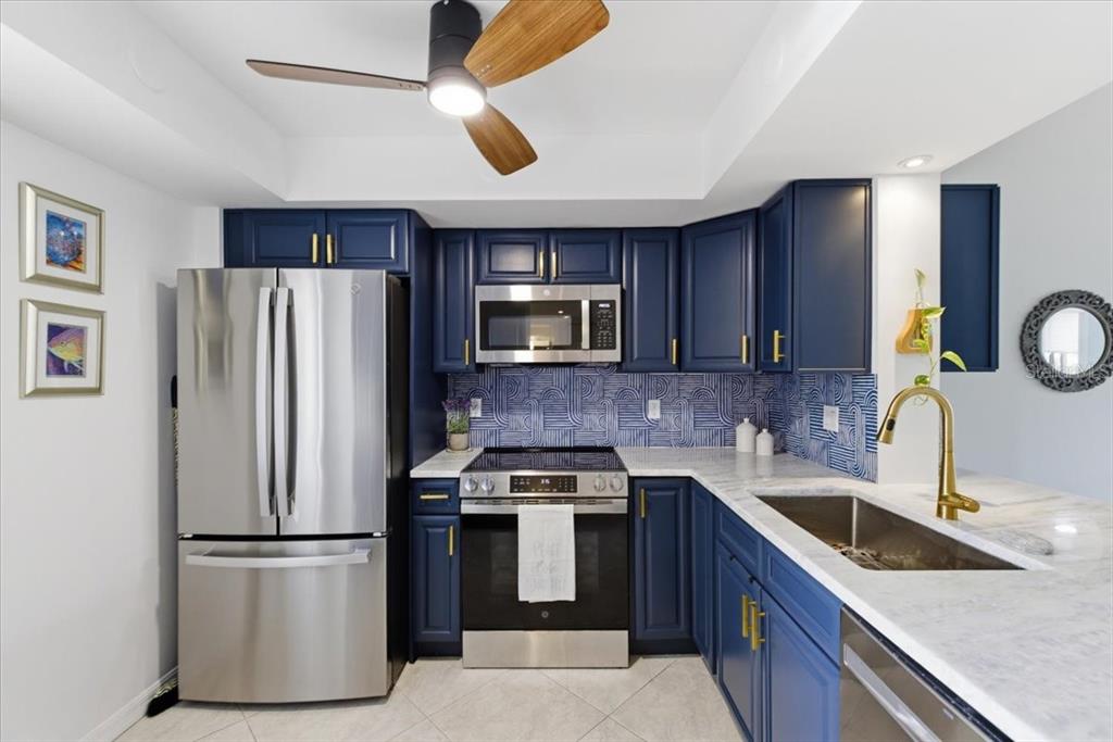 A kitchen features blue cabinets, stainless steel appliances, a patterned backsplash, and a ceiling fan — 2621 COVE CAY DRIVE UNIT 302, CLEARWATER, FL