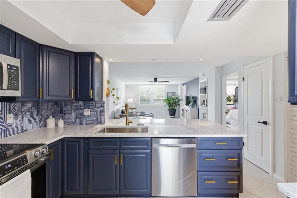 A kitchen features navy blue cabinets, gold hardware, patterned backsplash, and a white stone countertop — 2621 COVE CAY DRIVE UNIT 302, CLEARWATER, FL