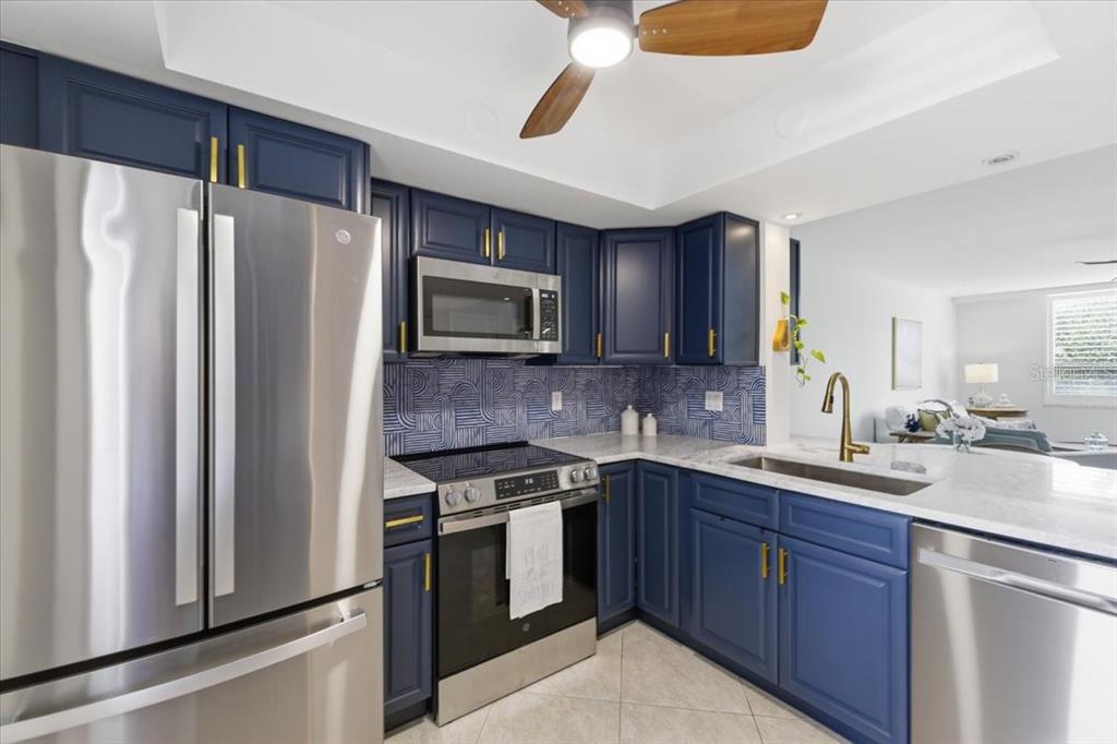 A kitchen features blue cabinets, stainless steel appliances, patterned backsplash tile, and a ceiling fan — 2621 COVE CAY DRIVE UNIT 302, CLEARWATER, FL