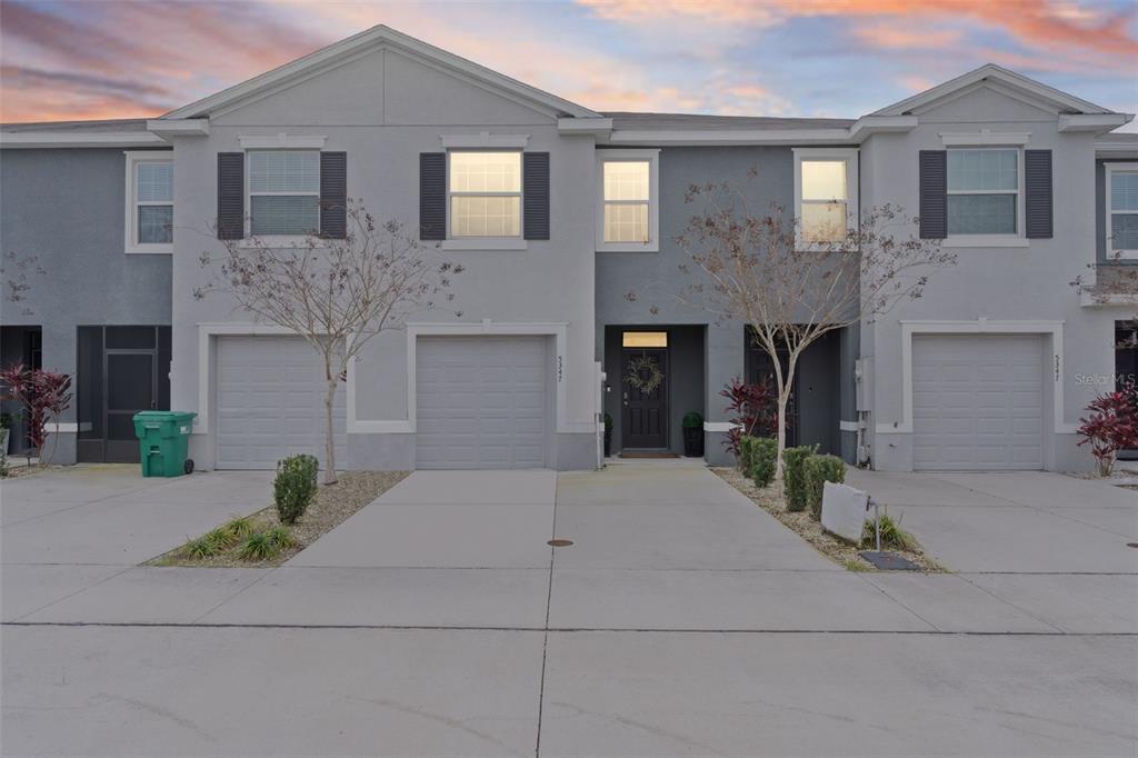 A two-story townhouse exterior features gray stucco walls, three garage doors, and a front entrance — 5349 PINECONE COURT, WILDWOOD, FL