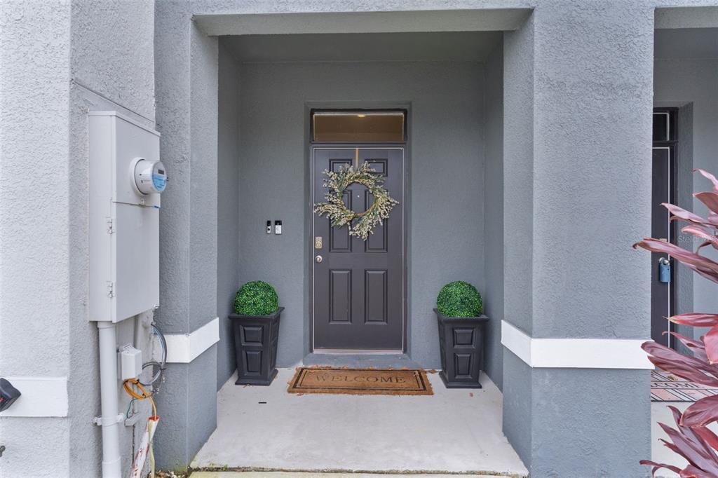 A dark front door with a wreath and two potted plants sits in a recessed entryway — 5349 PINECONE COURT, WILDWOOD, FL