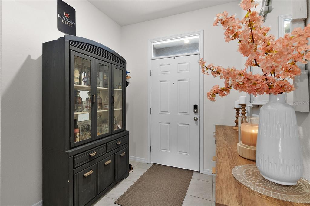 An entryway features a dark wood hutch, a white front door, and a floral arrangement — 5349 PINECONE COURT, WILDWOOD, FL