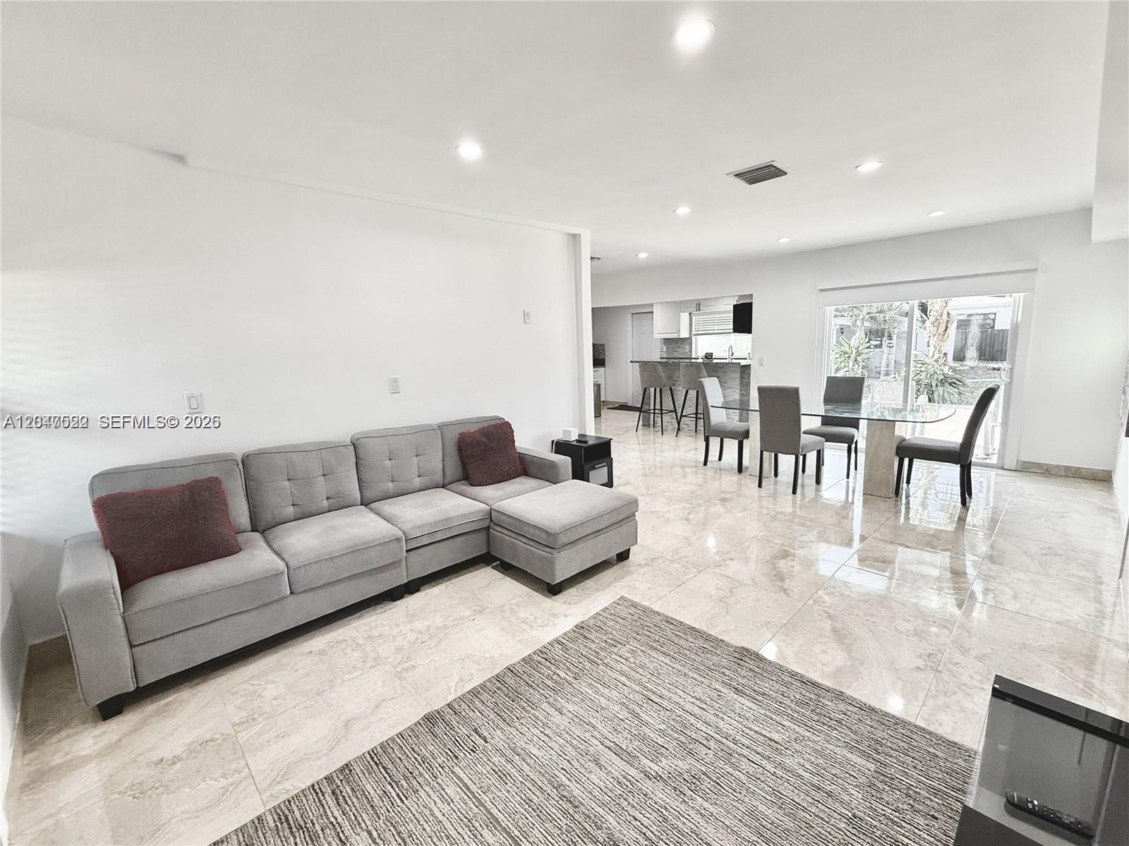 A living room with a grey sectional sofa, dining area, and light-colored tile flooring — 947 NE 149th st # 0, Miami FL 33161, MIAMI, FL