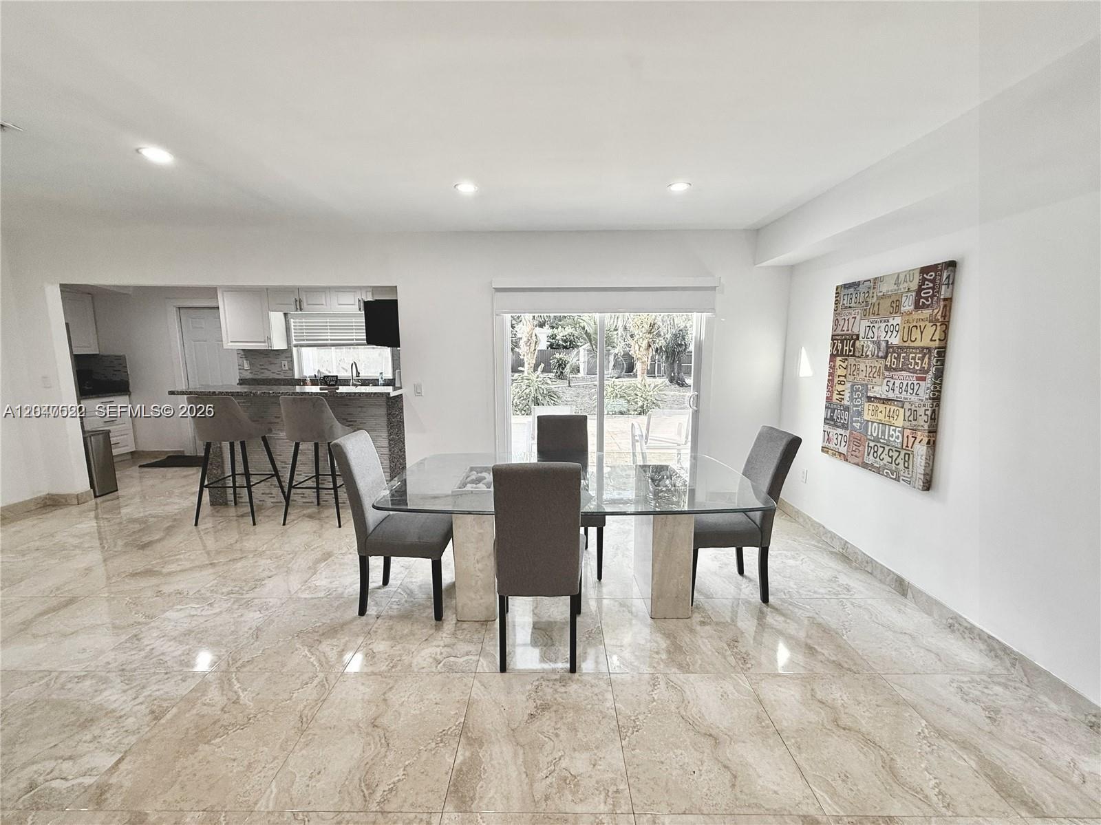 A dining area with a glass table and gray chairs sits before a sliding glass door — 947 NE 149th st # 0, Miami FL 33161, MIAMI, FL