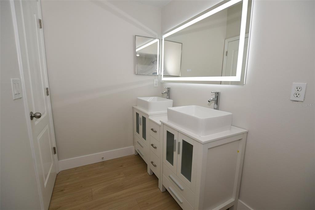 A bathroom features a double vanity with vessel sinks, a lighted mirror, and wood flooring — 12208 WILD IRIS WAY UNIT 112, ORLANDO, FL