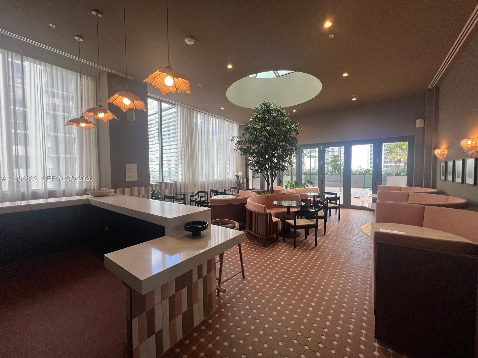 A lounge area features a bar, curved seating, a central tree, and floor-to-ceiling windows — 11 NE 6 ST # 2709, Miami FL 33132, MIAMI, FL