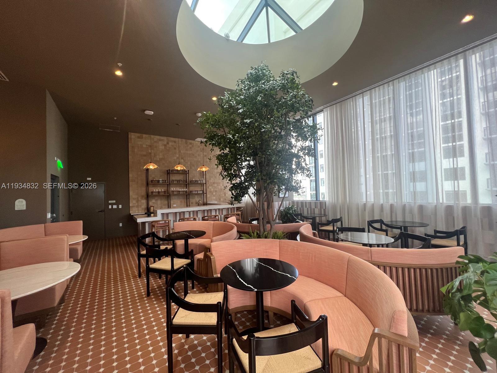 A lounge area features curved pink booths, round tables, a central tree, and a skylight — 11 NE 6 ST # 2709, Miami FL 33132, MIAMI, FL
