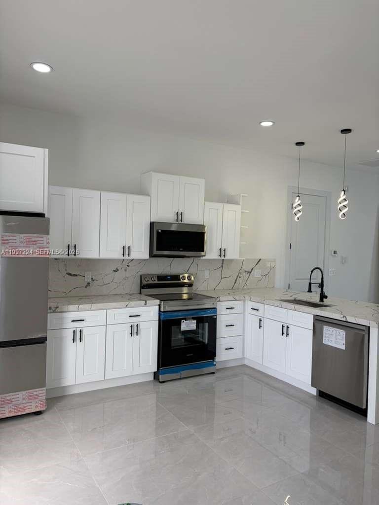 A modern kitchen features white cabinets, stainless steel appliances, and marble-patterned countertops and backsplash — 726 Clancy St E, Lehigh Acres FL 33974, LEHIGH ACRES, FL