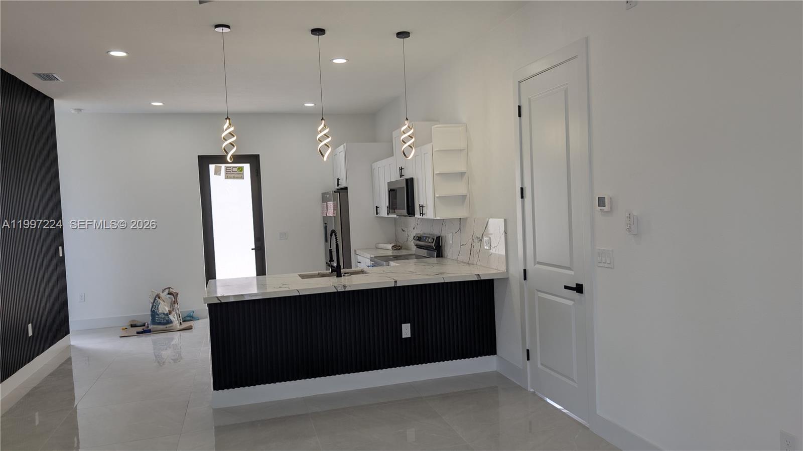 A modern kitchen features a black slatted island, white cabinetry, and marble-patterned countertops — 726 Clancy St E, Lehigh Acres FL 33974, LEHIGH ACRES, FL