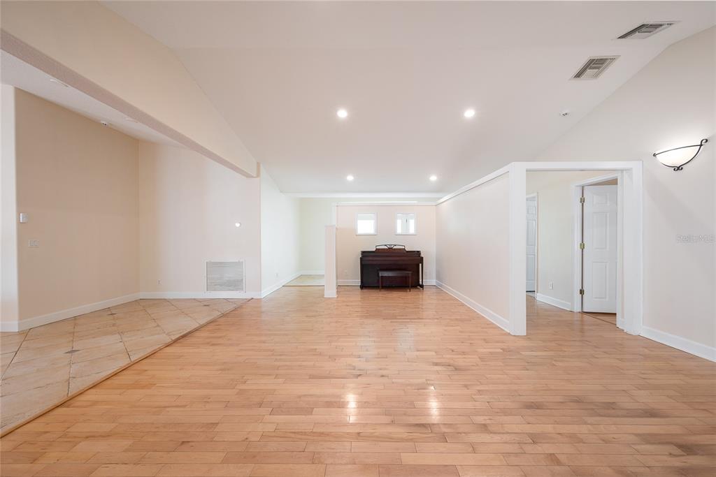 A spacious room features light wood flooring, a piano, and a tiled entryway area — 1015 VENETIAN AVENUE, ORLANDO, FL