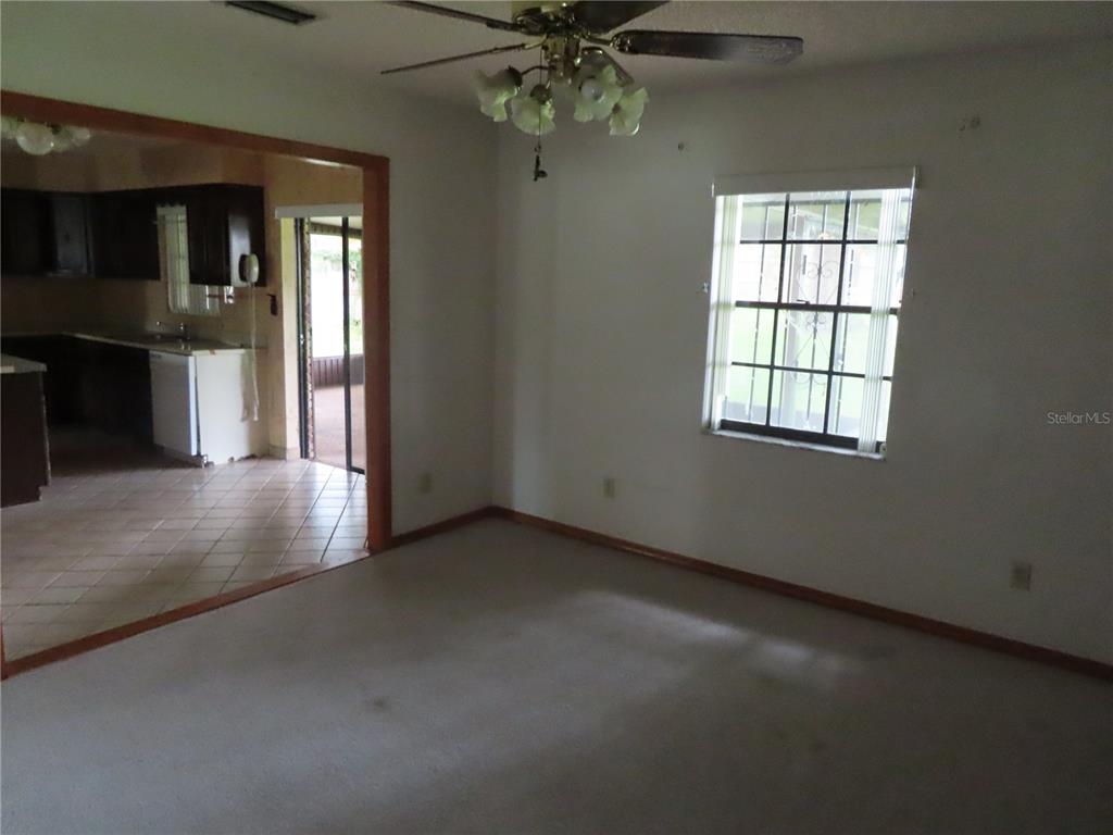 A carpeted living room with a ceiling fan connects to a tiled kitchen and patio — 2016 AMESBURY DRIVE, AUBURNDALE, FL