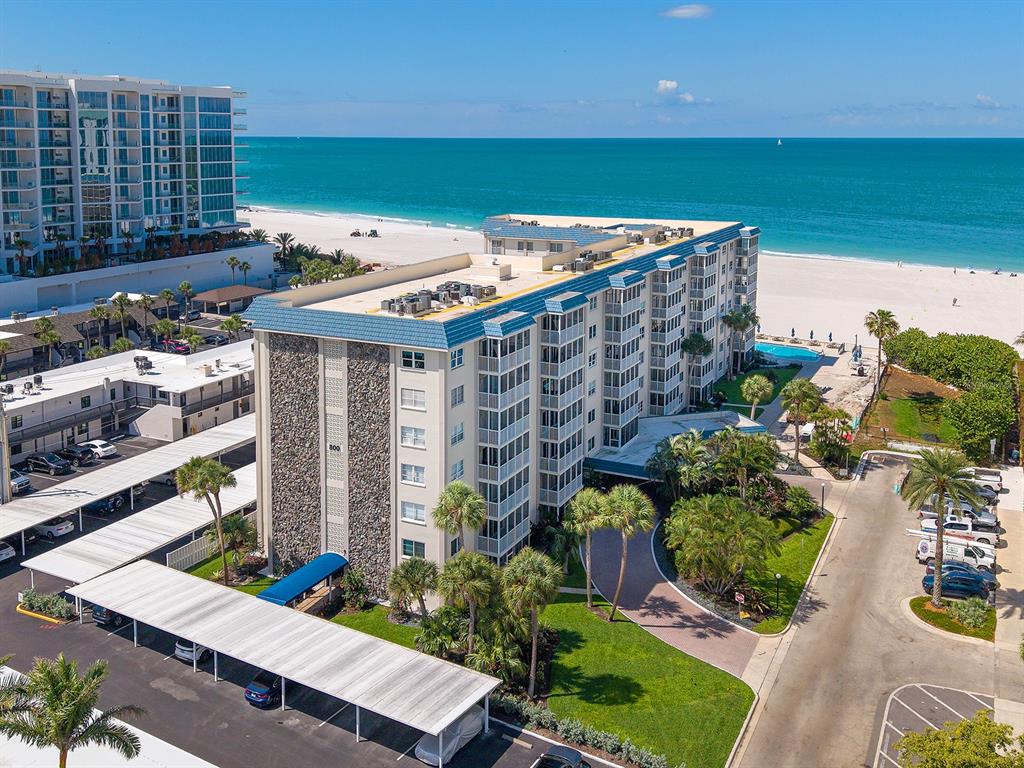 An aerial view shows a multi-story beachfront condominium building with covered parking and palm trees — 800 BENJAMIN FRANKLIN DRIVE UNIT 304, SARASOTA, FL