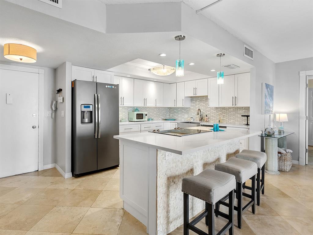 A modern kitchen features white cabinetry, a quartz island with bar seating, and stainless appliances — 800 BENJAMIN FRANKLIN DRIVE UNIT 304, SARASOTA, FL