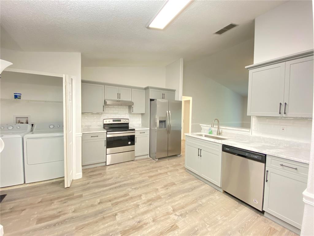 A kitchen with grey cabinets, stainless steel appliances, and light wood-look flooring — 13724 RIVERPATH GROVE DRIVE, ORLANDO, FL