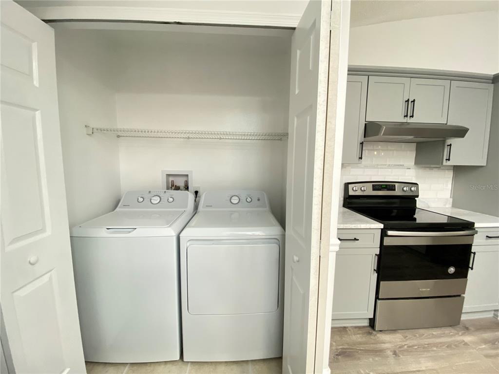 A laundry closet with a washer and dryer sits next to a kitchen with gray cabinets — 13724 RIVERPATH GROVE DRIVE, ORLANDO, FL