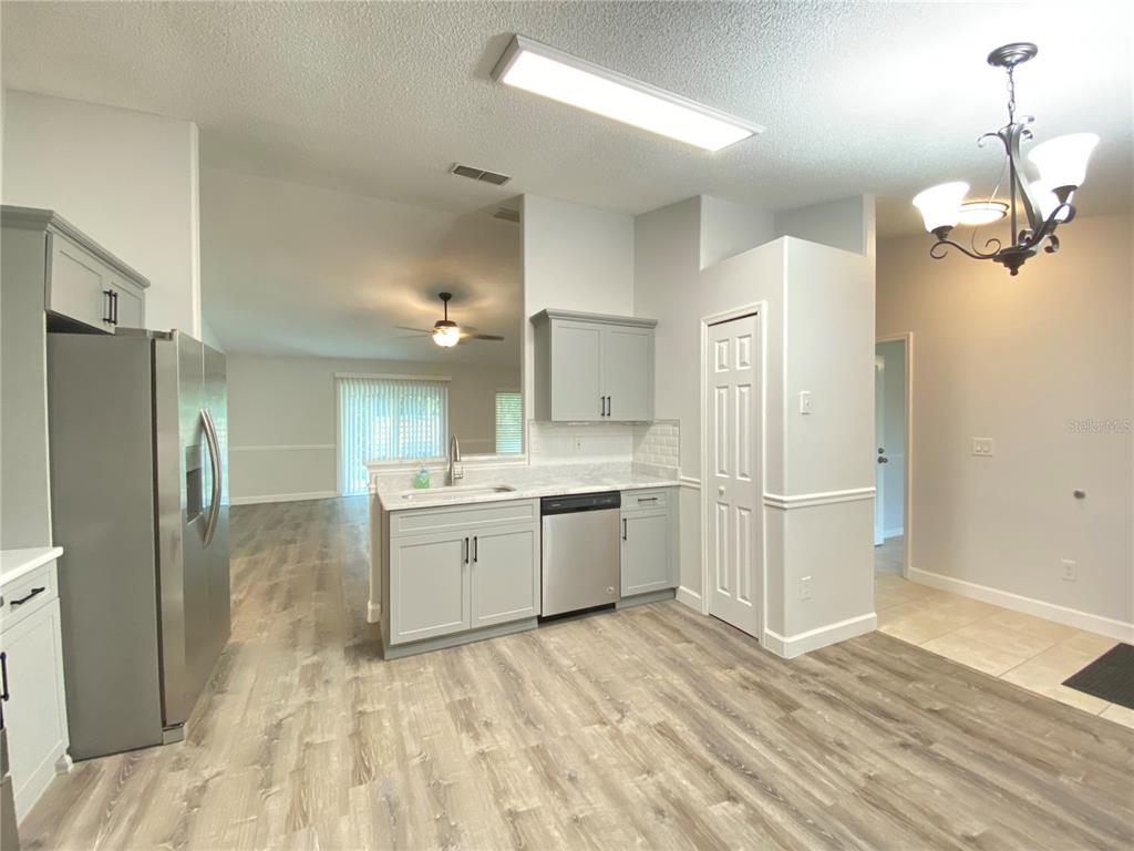 A kitchen with gray cabinets, stainless steel appliances, and wood-look flooring opens to a living area — 13724 RIVERPATH GROVE DRIVE, ORLANDO, FL