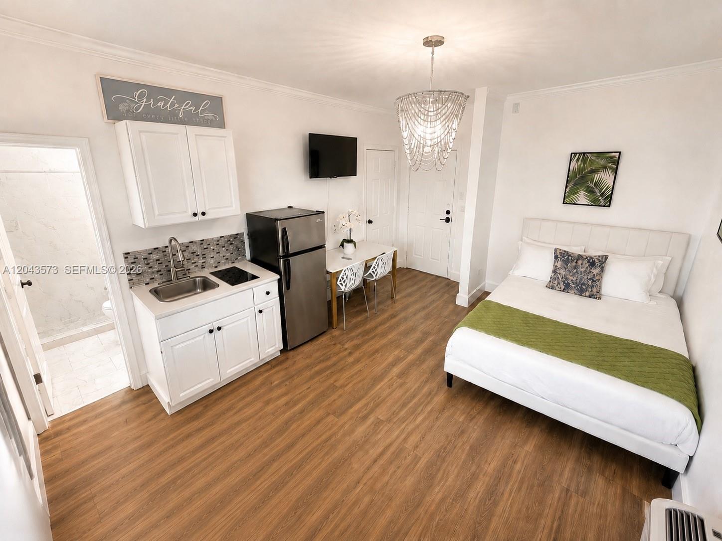 A studio apartment features a kitchenette, a bed, and a dining area with wood flooring — 3025 Indian Creek Dr # 322, Miami Beach FL 33140, MIAMI BEACH, FL