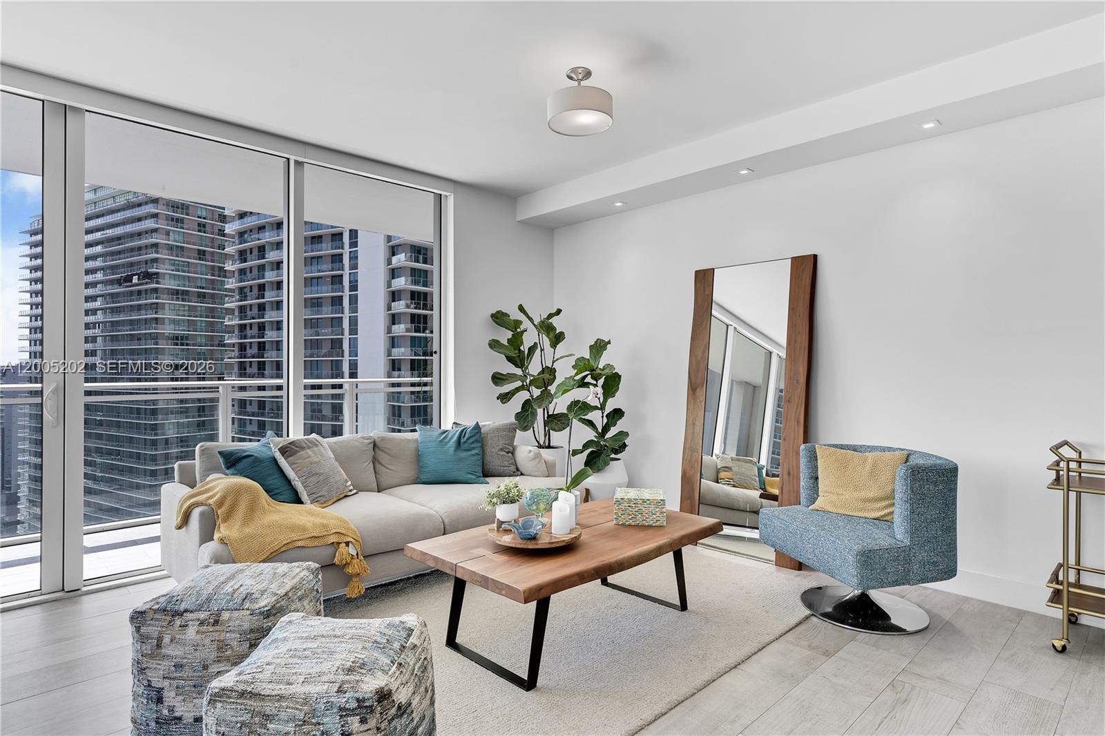 A modern living room features a grey sofa, blue accent chair, and floor-to-ceiling windows — 1080 Brickell Ave # 2601, Miami FL 33131, MIAMI, FL