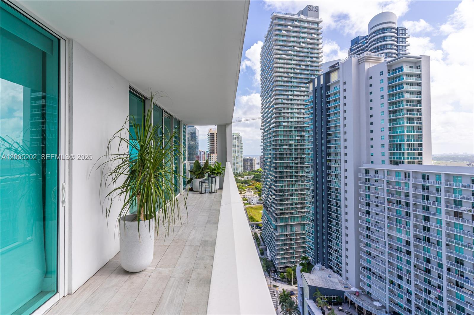 A high-rise balcony features a potted plant, wood-look tile flooring, and views of city skyscrapers — 1080 Brickell Ave # 2601, Miami FL 33131, MIAMI, FL