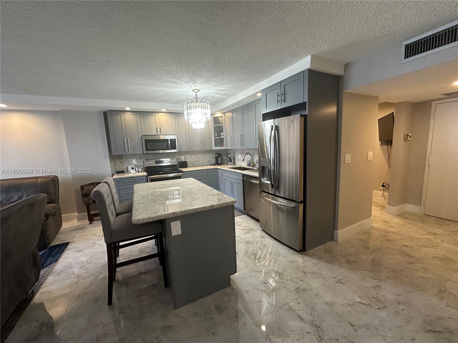 A kitchen features gray cabinetry, stainless steel appliances, a granite island, and marble-style flooring — 1865 S Ocean Dr # 17C, Hallandale Beach FL 33009, HALLANDALE BEACH, FL