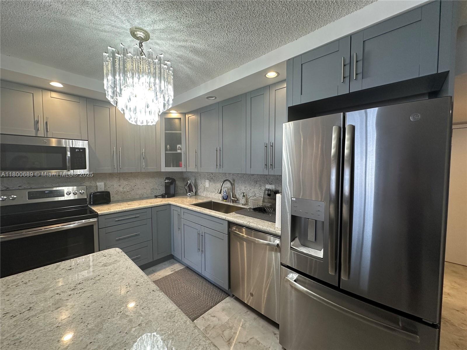 A kitchen features gray cabinets, stainless steel appliances, and granite countertops under a crystal chandelier — 1865 S Ocean Dr # 17C, Hallandale Beach FL 33009, HALLANDALE BEACH, FL
