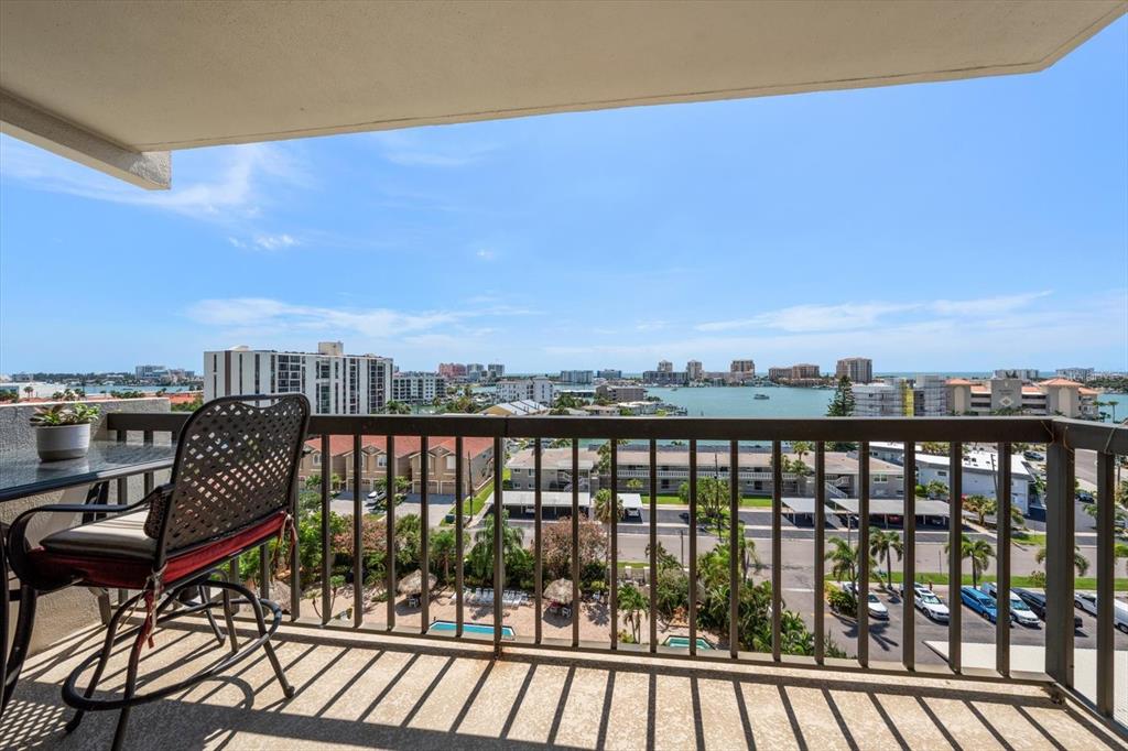 A balcony with a metal railing overlooks a parking lot, residential buildings, and a bay — 400 ISLAND WAY UNIT 904, CLEARWATER BEACH, FL