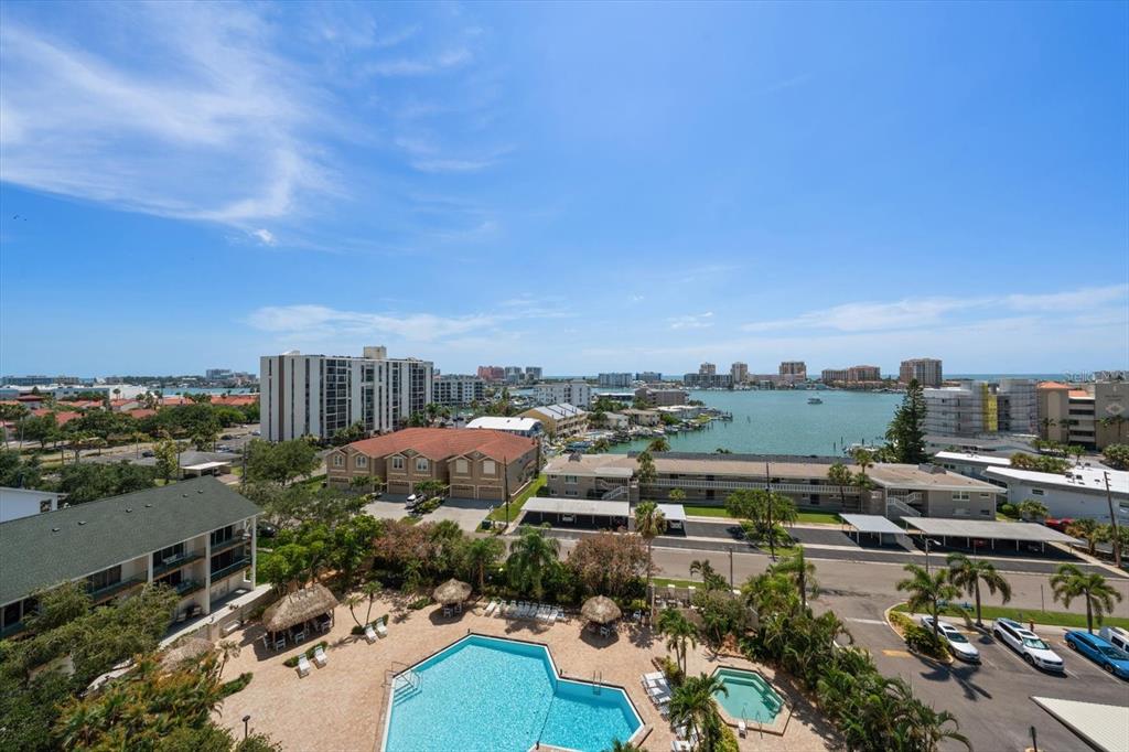 An elevated view of a swimming pool, surrounding buildings, and a bay under a blue sky — 400 ISLAND WAY UNIT 904, CLEARWATER BEACH, FL