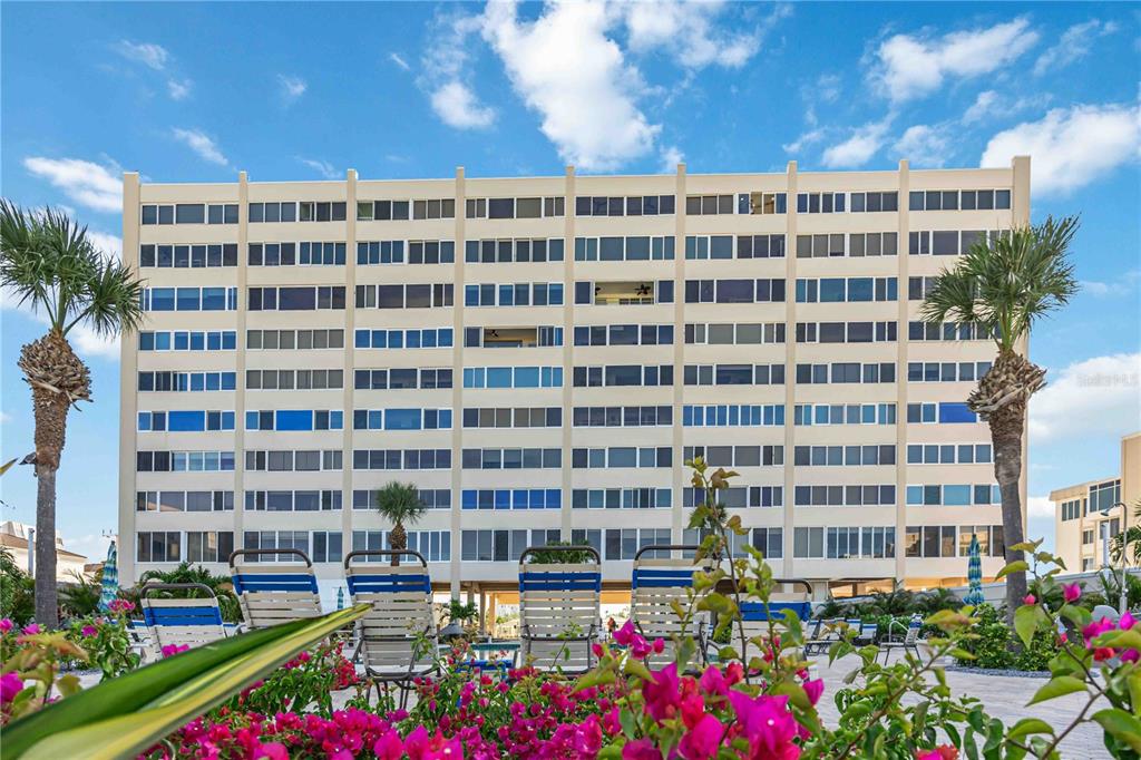 A multi-story apartment building stands behind a pool deck with lounge chairs and flowering plants — 6140 MIDNIGHT PASS ROAD UNIT 606, SARASOTA, FL