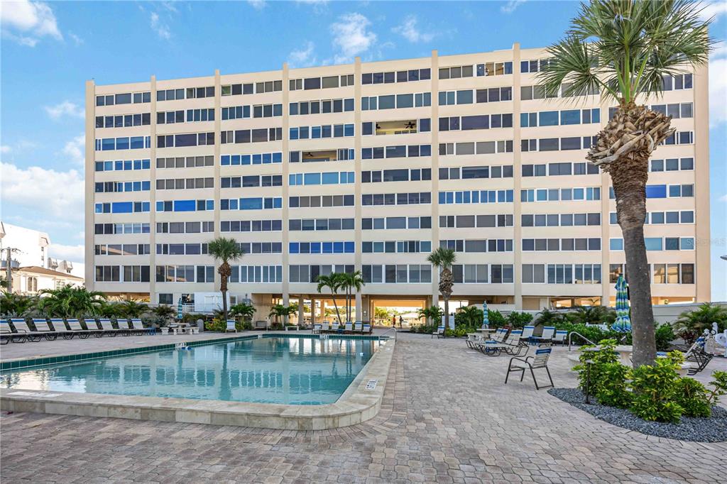 A multi-story apartment building stands behind a swimming pool and a paved patio area — 6140 MIDNIGHT PASS ROAD UNIT 606, SARASOTA, FL