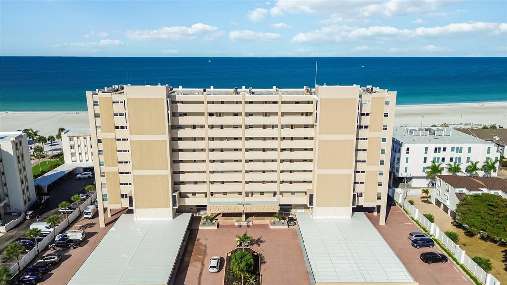 An aerial view of a multi-story beachfront condominium building with covered parking and surrounding landscaping — 6140 MIDNIGHT PASS ROAD UNIT 606, SARASOTA, FL