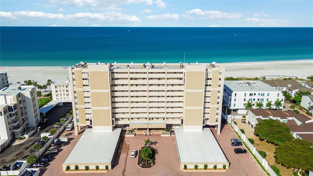 An aerial view of a multi-story beachfront condominium building with parking areas and surrounding landscaping — 6140 MIDNIGHT PASS ROAD UNIT 606, SARASOTA, FL