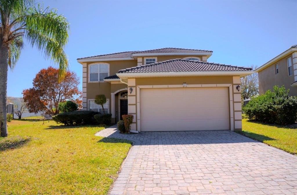 A two-story house with a tan stucco exterior, a tile roof, and a paved driveway — 416 VISTA LOOP, DAVENPORT, FL