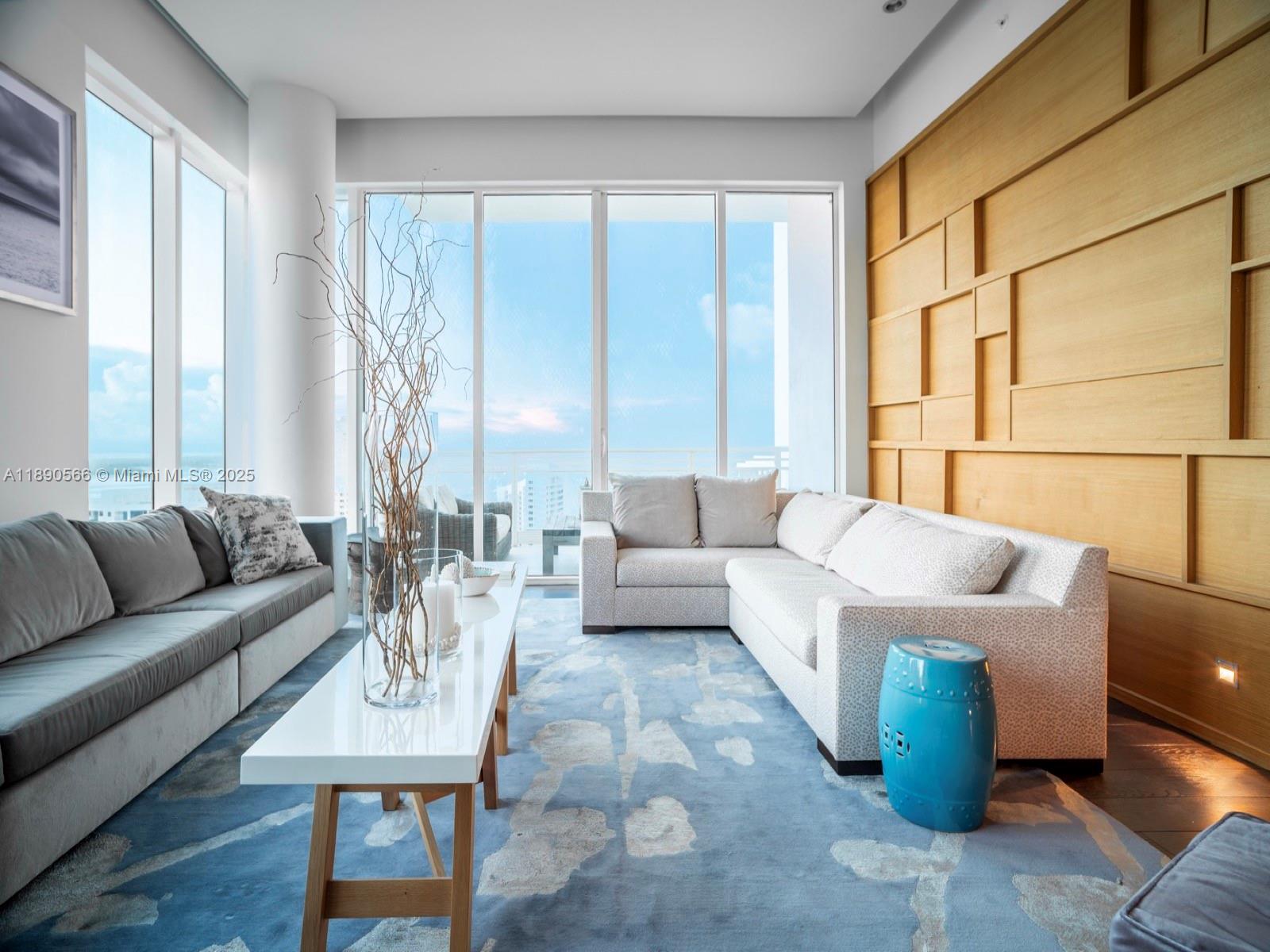 A living room features a sectional sofa, a blue patterned rug, and wood-paneled walls — 900 Brickell Key Blvd # 2204, Miami FL 33131, MIAMI, FL
