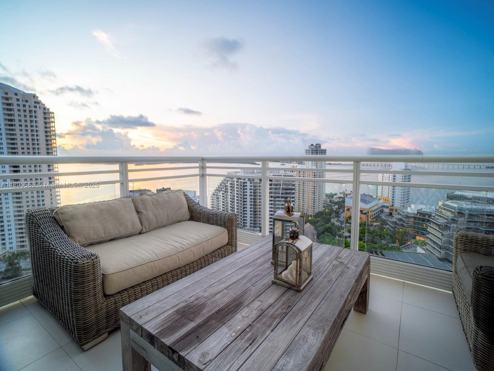 A balcony features a wicker sofa and wooden coffee table overlooking a city skyline — 900 Brickell Key Blvd # 2204, Miami FL 33131, MIAMI, FL