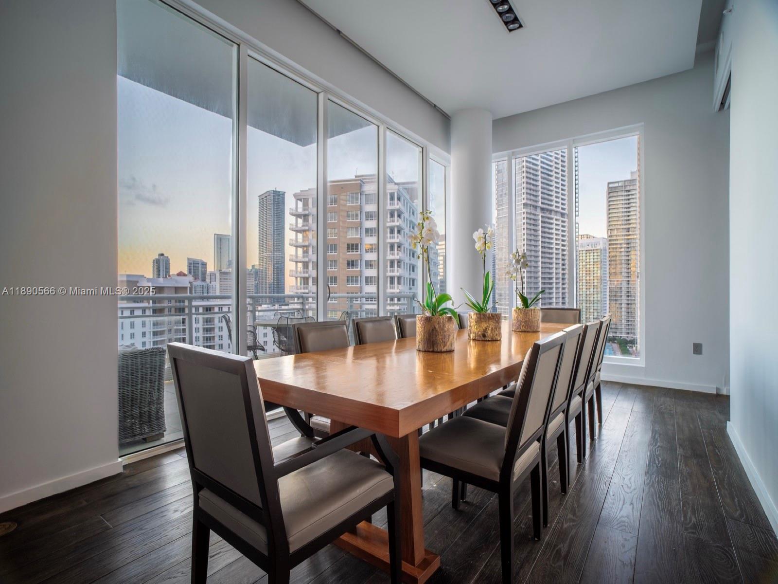 A dining room features a wooden table, grey chairs, and floor-to-ceiling windows with city views — 900 Brickell Key Blvd # 2204, Miami FL 33131, MIAMI, FL