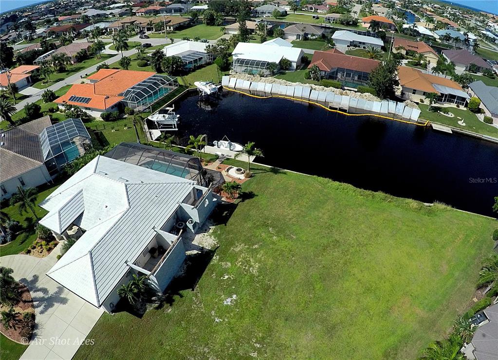 An aerial view shows a waterfront house with a pool cage and a large grassy lot — 631 COMO COURT, PUNTA GORDA, FL