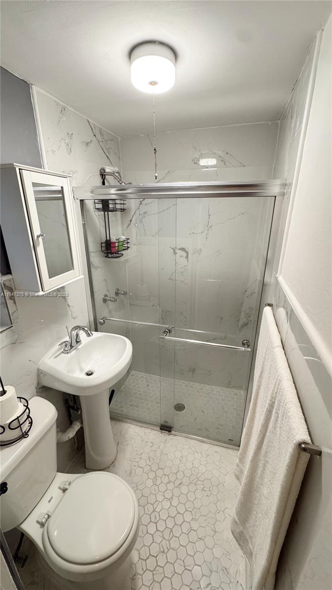 A small bathroom features a pedestal sink, a toilet, and a glass-enclosed shower stall — 460 NW 109th St, Miami FL 33168, MIAMI, FL