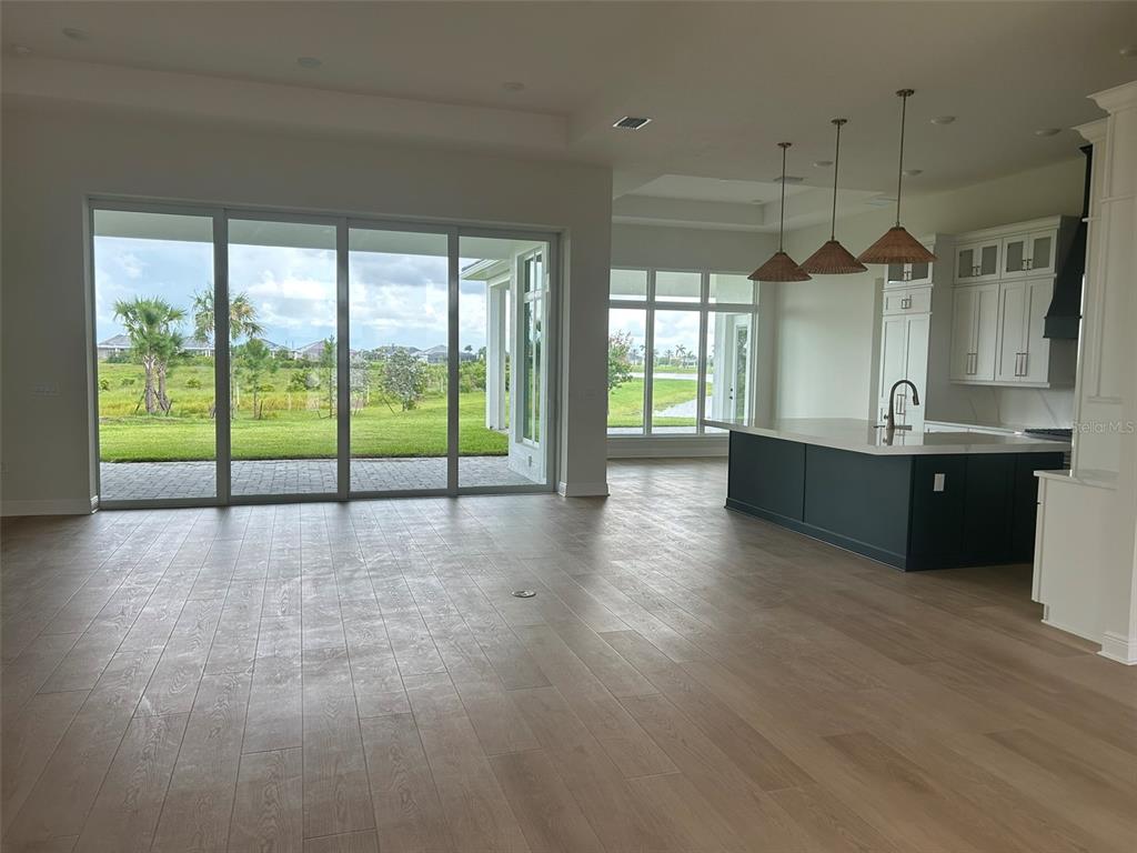 An open-concept kitchen and living area features light wood flooring, a dark island, and sliding glass doors — 17483 MONTGOMERY COURT, VENICE, FL