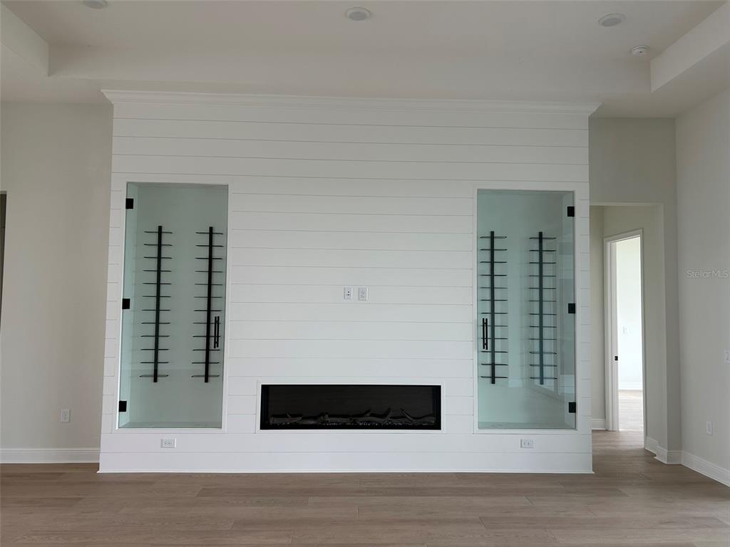 A living room wall features white shiplap, a linear fireplace, and two glass-enclosed wine displays — 17483 MONTGOMERY COURT, VENICE, FL