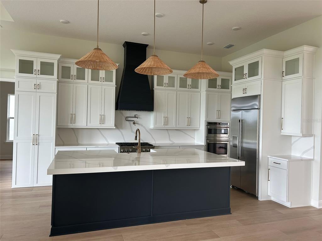 A modern kitchen features a dark blue island, white cabinetry, stainless steel appliances, and woven pendants — 17483 MONTGOMERY COURT, VENICE, FL