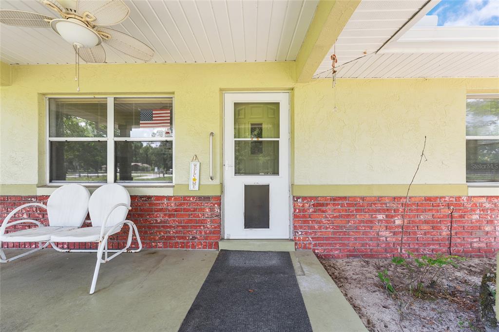 A covered porch features a white metal bench, a ceiling fan, and a brick facade — 7360 SW 15TH PLACE, OCALA, FL